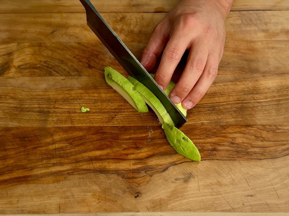 Avocado being sliced into wedges on a chopping board.