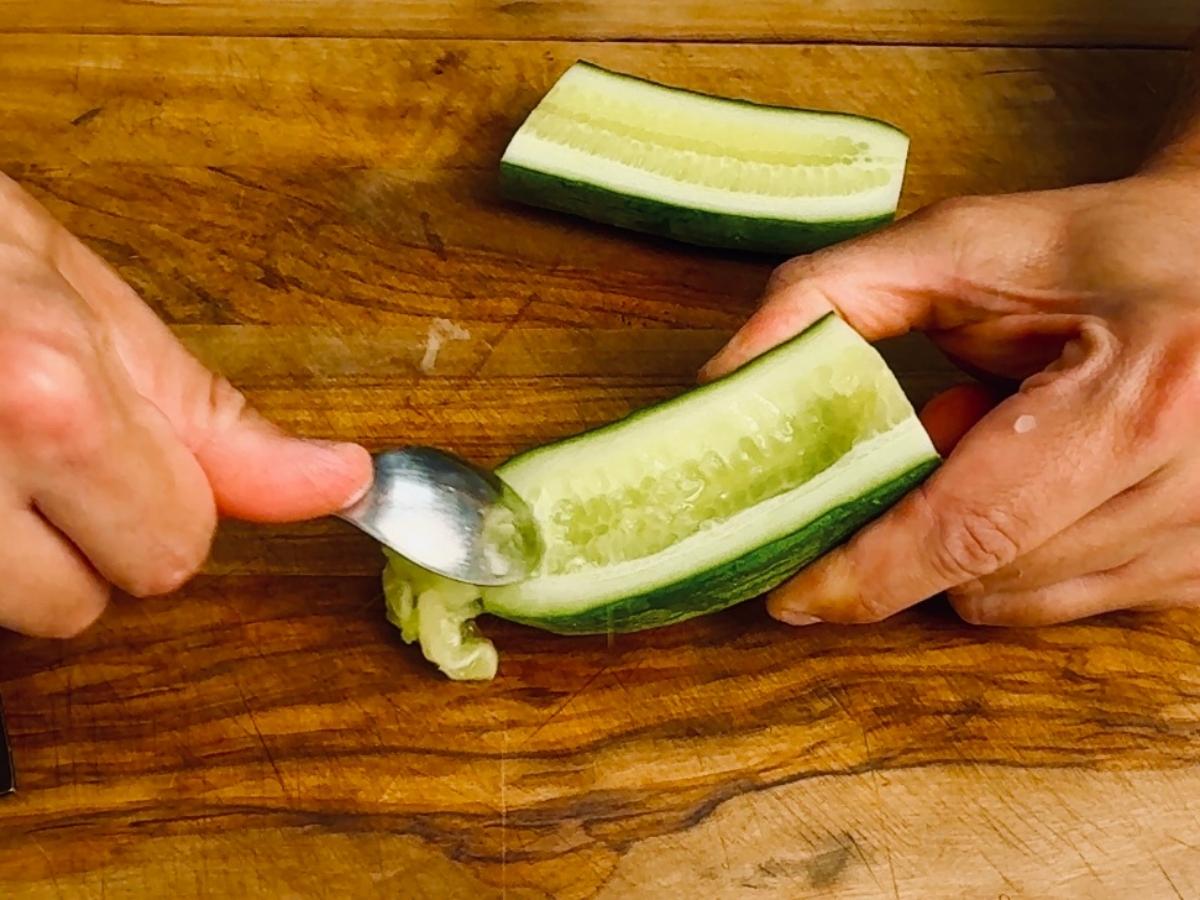 Spoon scooping out seeds from a halved cucumber.