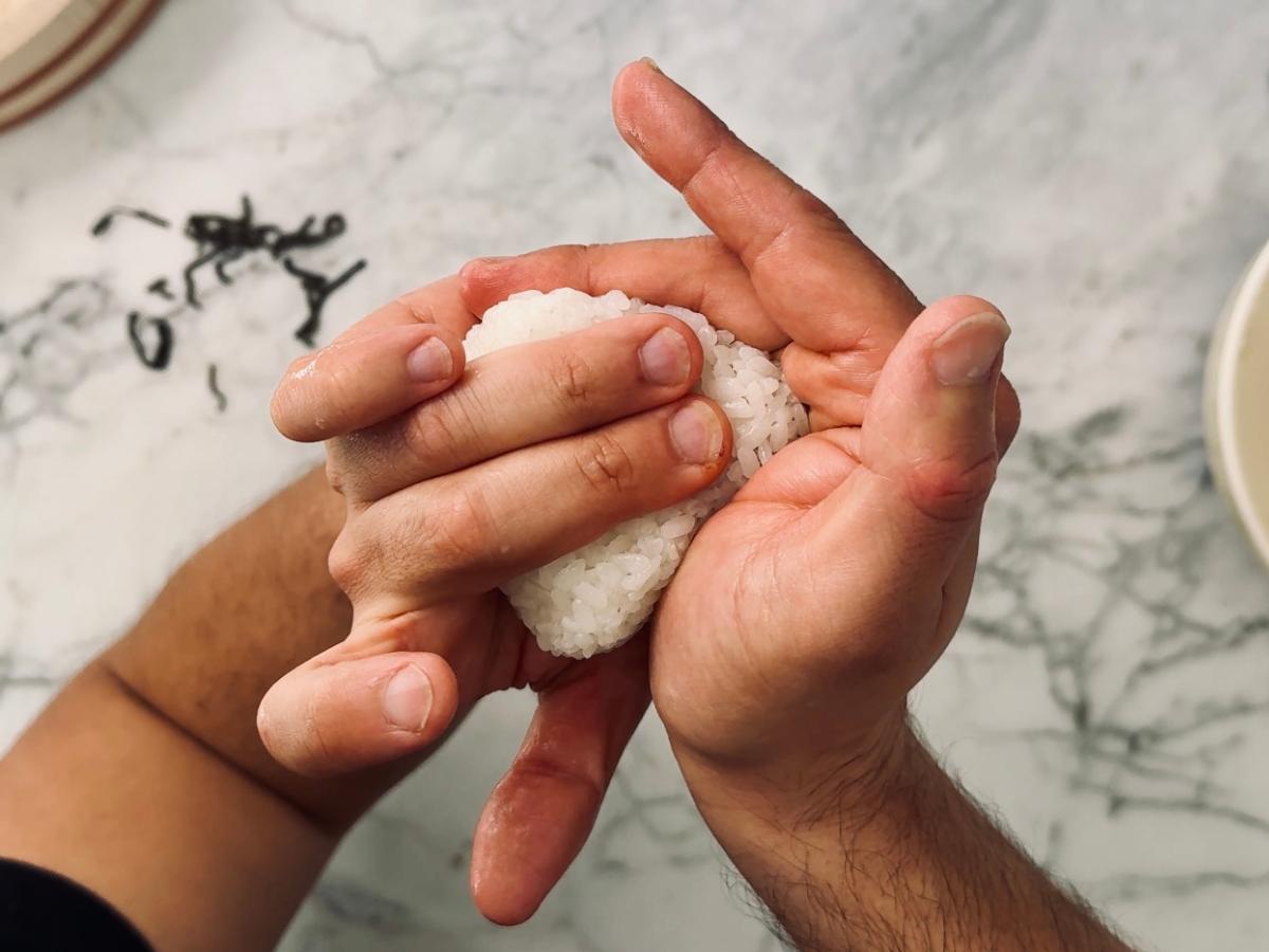 hands shaping onigiri vegan rice ball into a triangle.