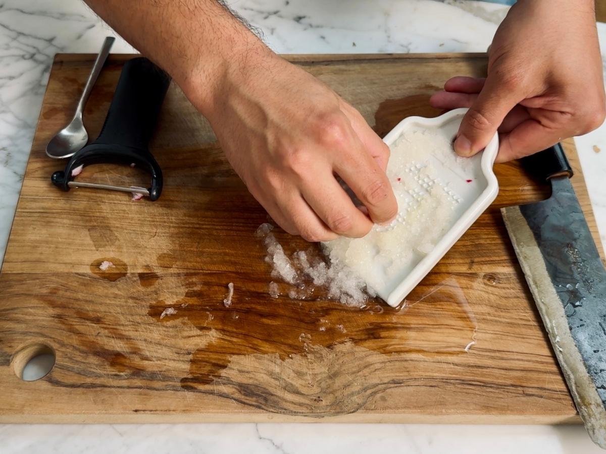 Peeled red radishes being grated on a fine grater.
