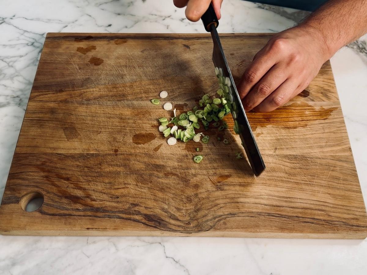 Spring onions sliced into thin rounds on a wooden board.