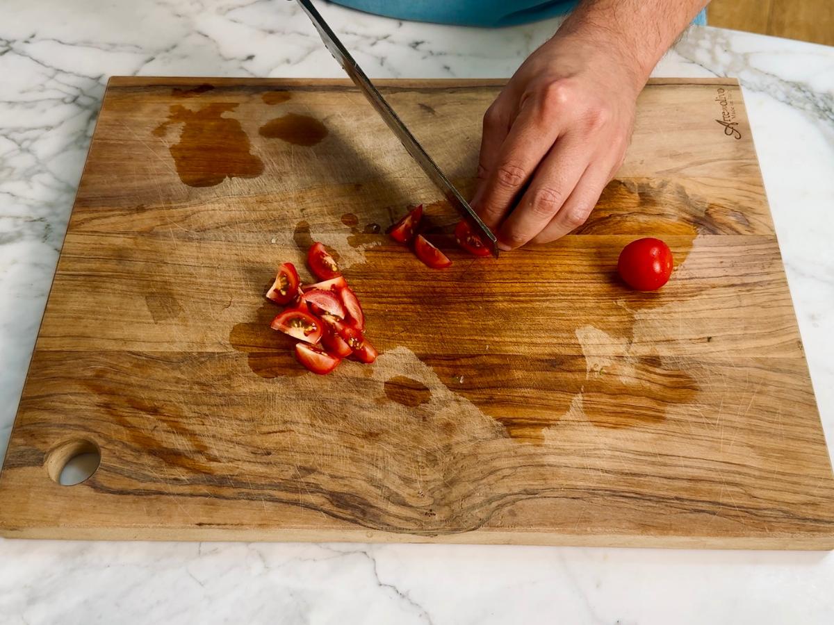 Cherry tomatoes cut into eighths on a wooden chopping board