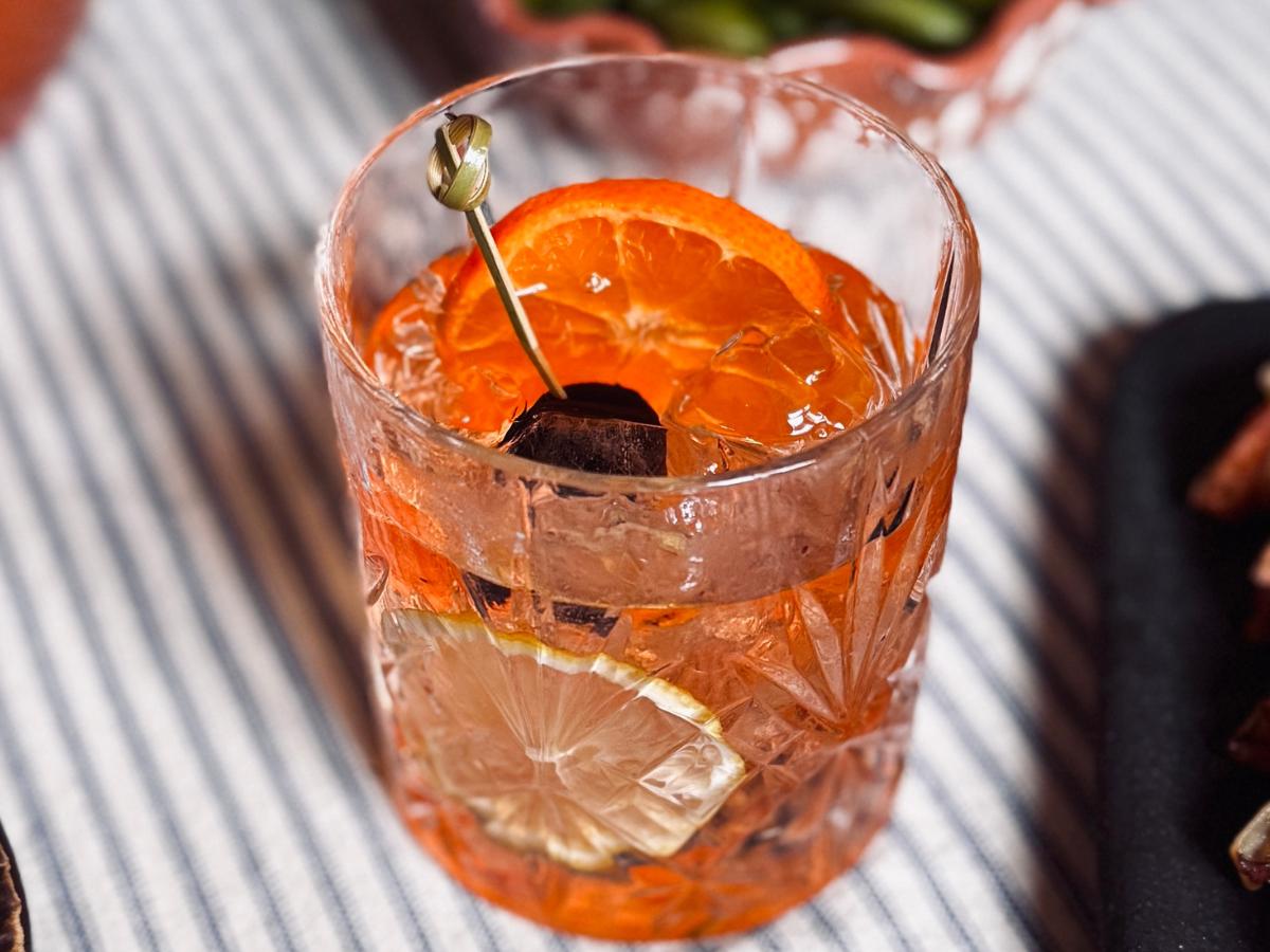 Sake old fashioned cocktail garnished with an orange slice and maraschino cherry, ready to serve