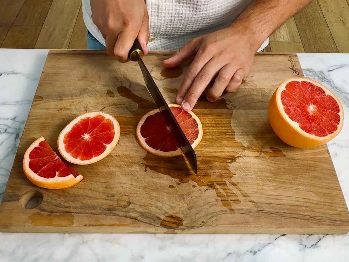 Sliced pink grapefruit into thin half-moon shapes on a cutting board.


