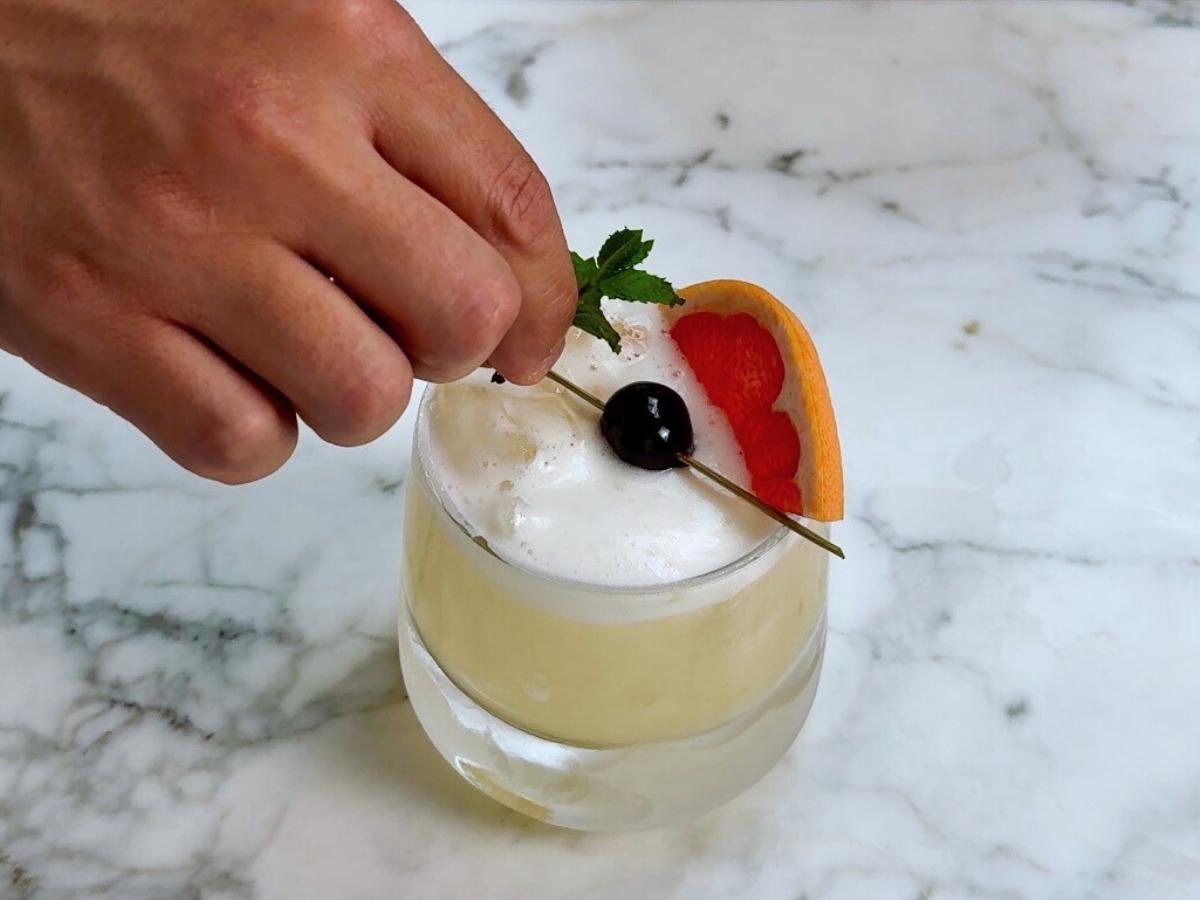 Finished spicy sake sour cocktail garnished with grapefruit, mint, and cherry.

