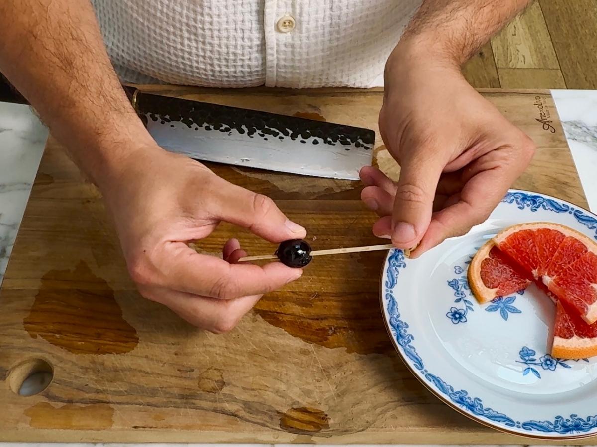 Hand skewering a bright red maraschino cherry with a cocktail pick.


