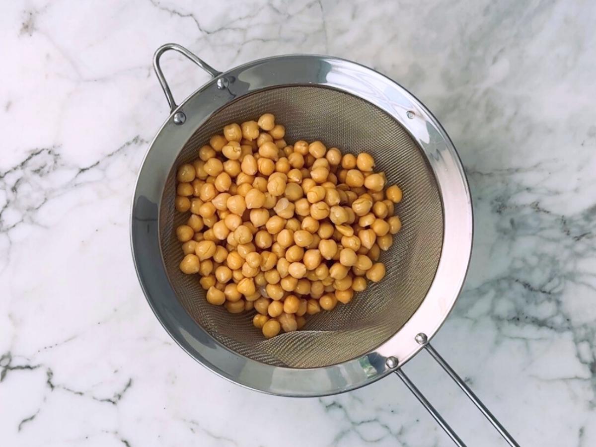 Chickpeas being strained over a bowl with aquafaba collecting below.

