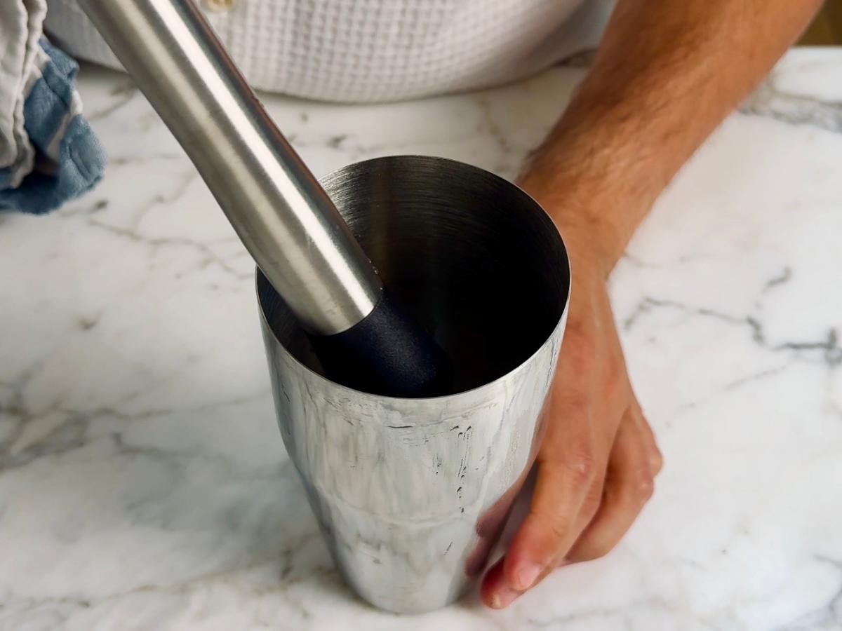 Muddling chopped red chilli, lemon juice, and agave nectar in a cocktail shaker.


