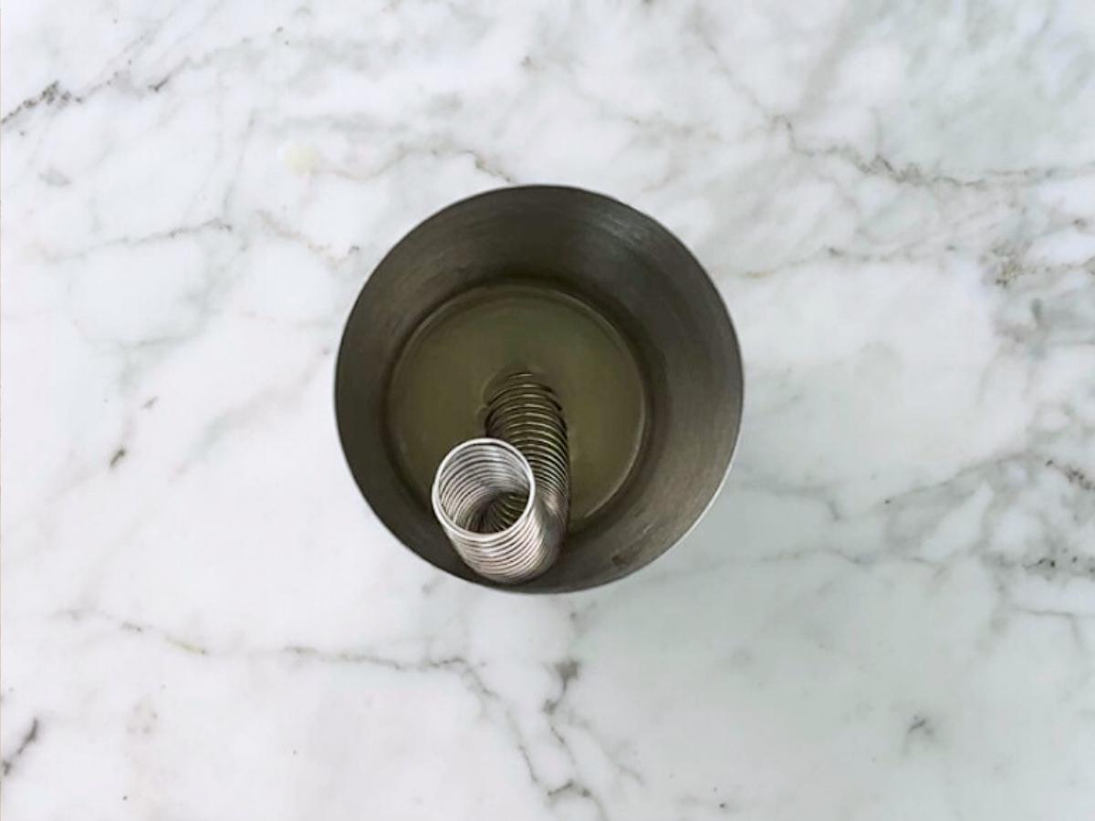 Aquafaba and sake in a shaker with a Hawthorne strainer spring inside it.