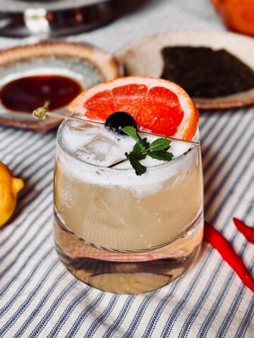 Sake sour garnished with cherry, mint and grapefruit on a stripey table cloth