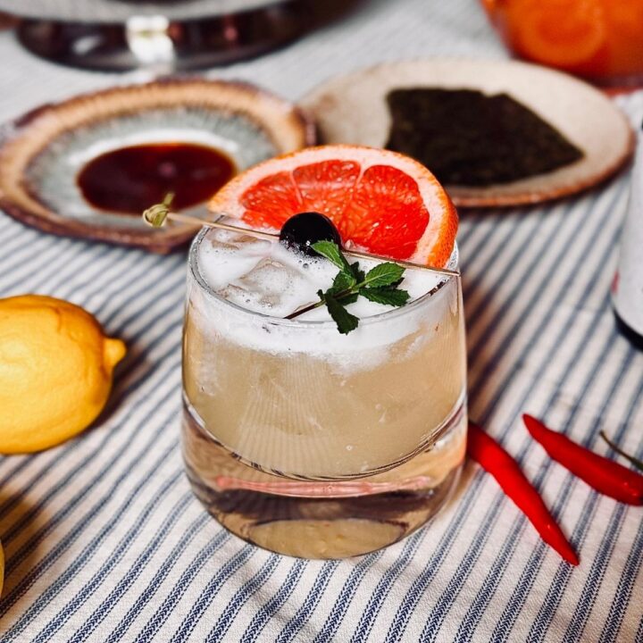 Sake sour garnished with cherry, mint and grapefruit on a stripey table cloth