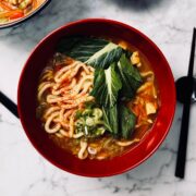 Curry udon noodles in a ramen bowl garnished with spring onions and choi sum