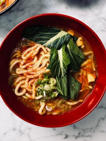 Curry udon noodles in a ramen bowl garnished with spring onions and choi sum leaves