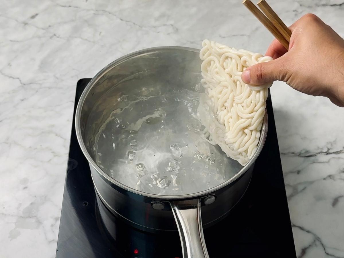 fresh udon noodles being placed into boiling water