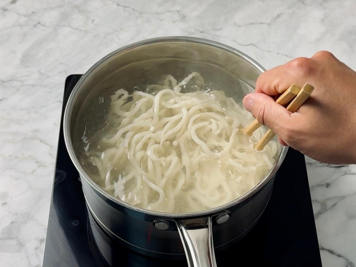 fresh udon noodles being seperated and stirred in hot water