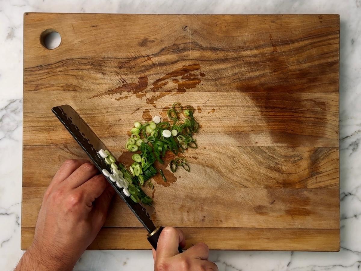 spring onions being sliced into thin rounds on a chopping board