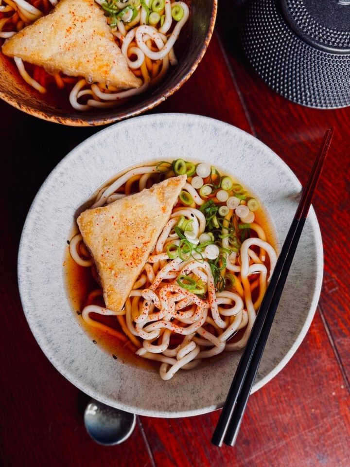 a bowl of kake udon (thick udon noodles in a translucent soy based broth) Topped with spring onions, crispy tofu and shichimi togarashi.