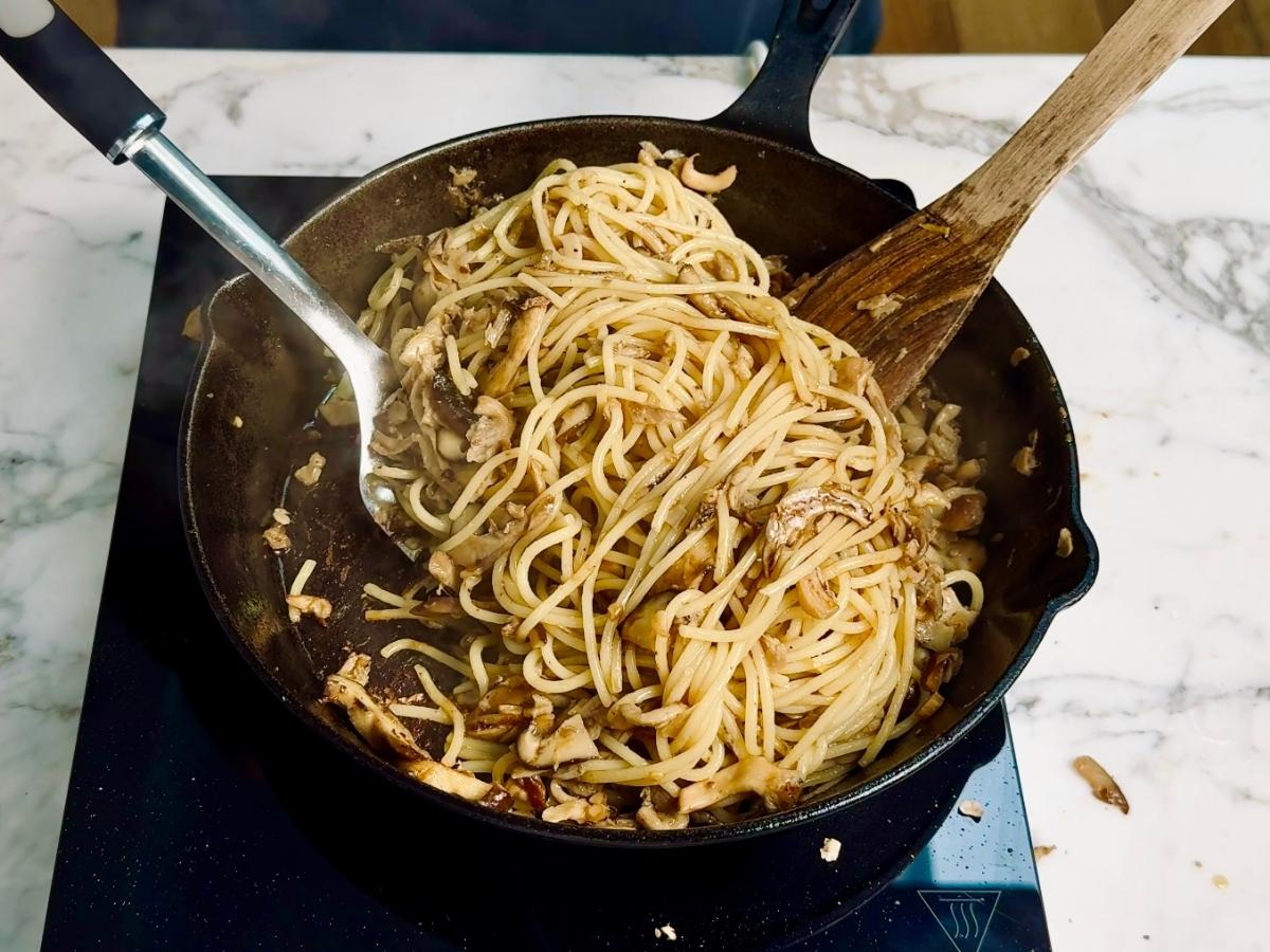 Cooked spaghetti tossed into the mushroom miso sauce in a frying pan.