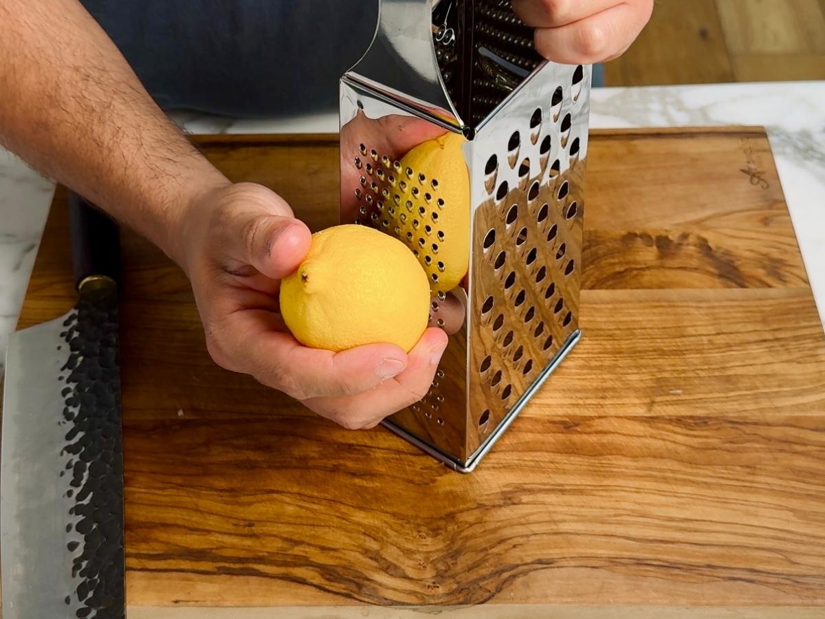 Lemon being zested with the fine side of a box grater.