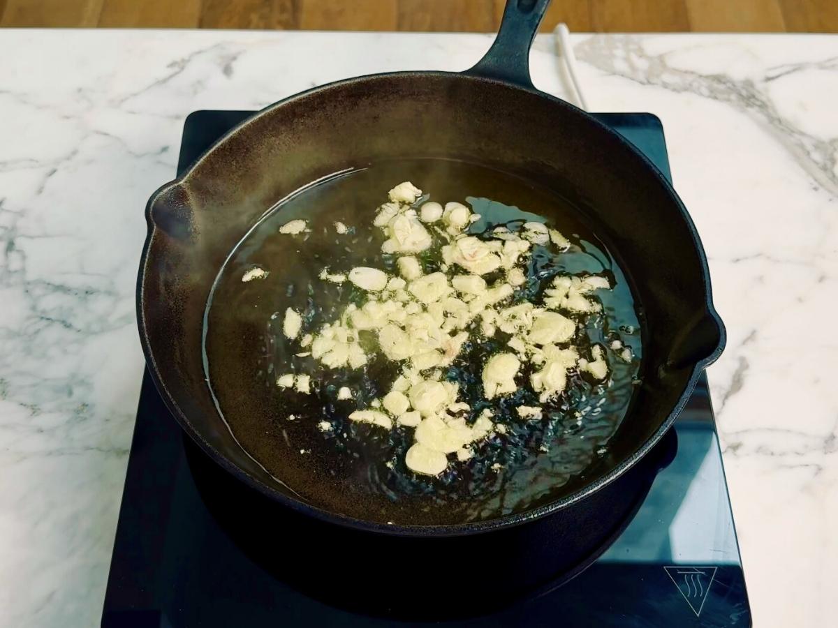 Garlic slices sizzling in olive oil in a hot frying pan.