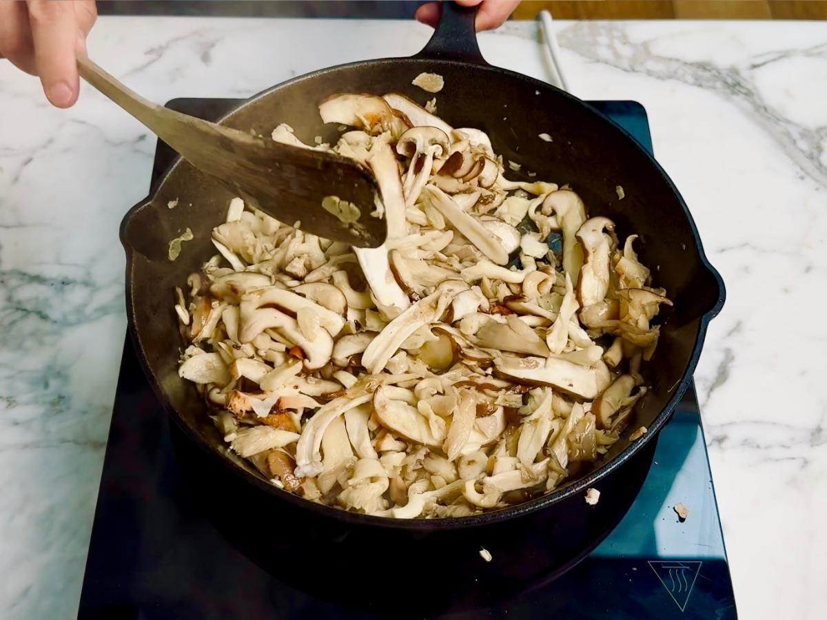 Mushrooms frying in a pan with garlic, butter, and miso sauce starting to coat them.