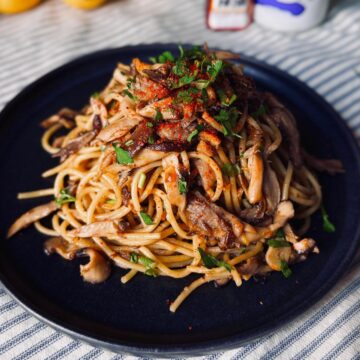 miso mushroom pasta on a round ceramic plate garnished with shichimi togarashi spice and parsley
