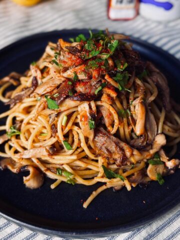 miso mushroom pasta on a round ceramic plate garnished with shichimi togarashi spice and parsley