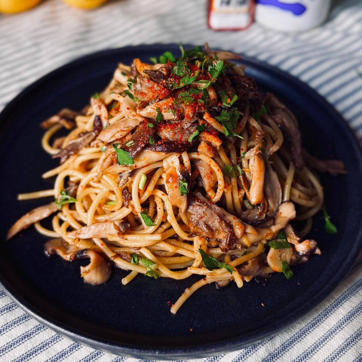 miso mushroom pasta on a round ceramic plate garnished with shichimi togarashi spice and parsley