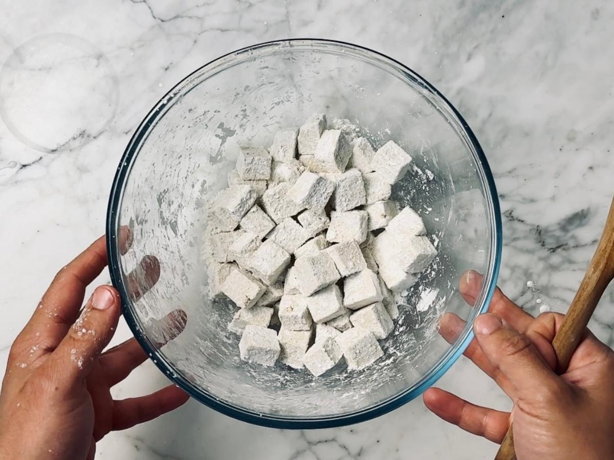 tofu in a mixing bowl being coated with cornstarch