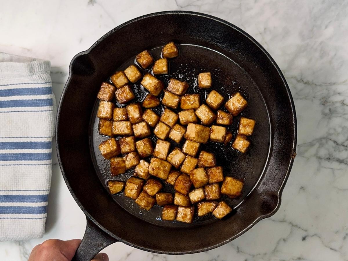 tofu pieces being coated with sauces, browned in a skillet