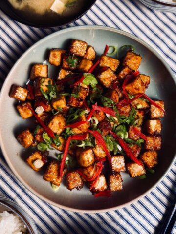 sticky tofu on a round plate garnished with spring onions and pickled ginger