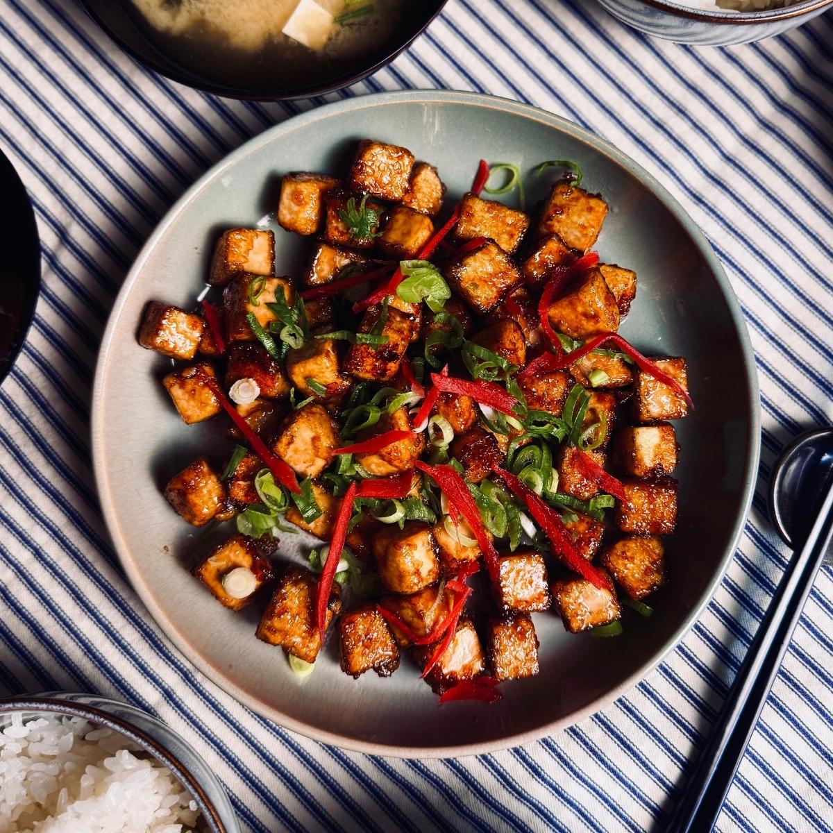 sticky tofu on a round plate garnished with spring onions and pickled ginger