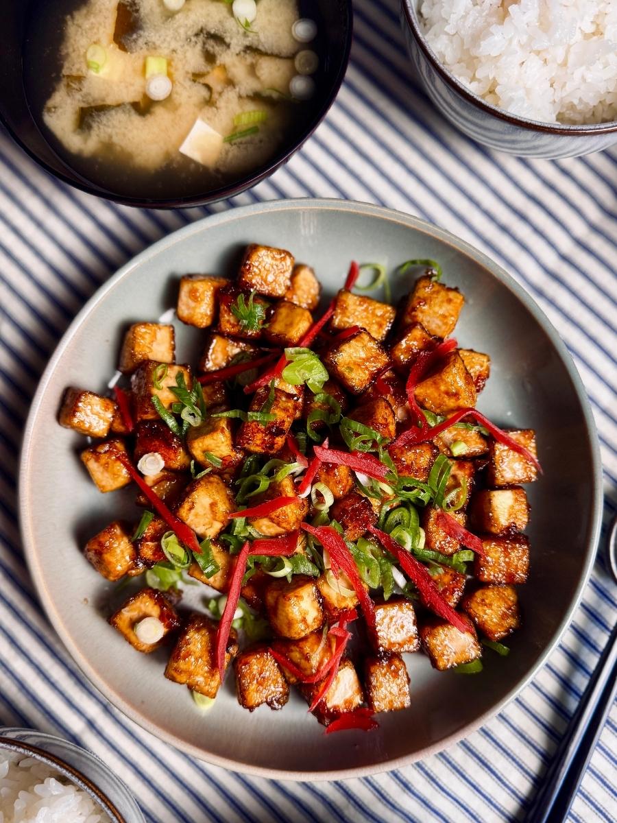 sticky tofu on a round plate garnished with spring onions and pickled ginger next to miso soup and rice