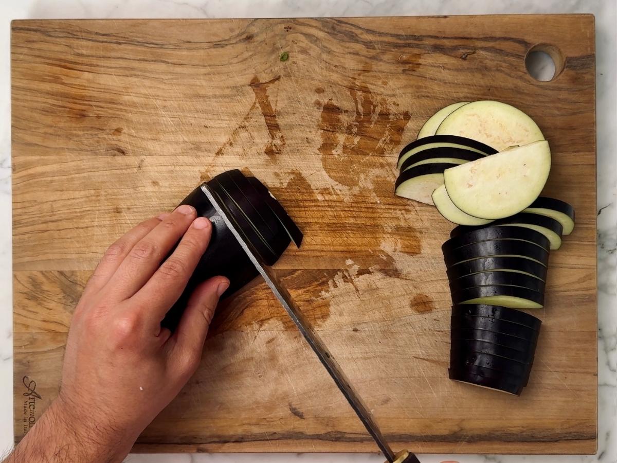 haved eggplant being chopped into thin half moon slices