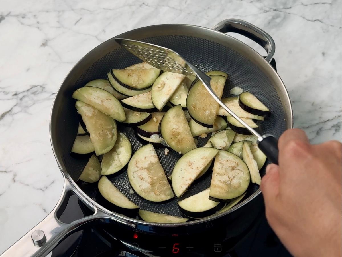 egglant slices bing tossed in a frying pan with the garlic