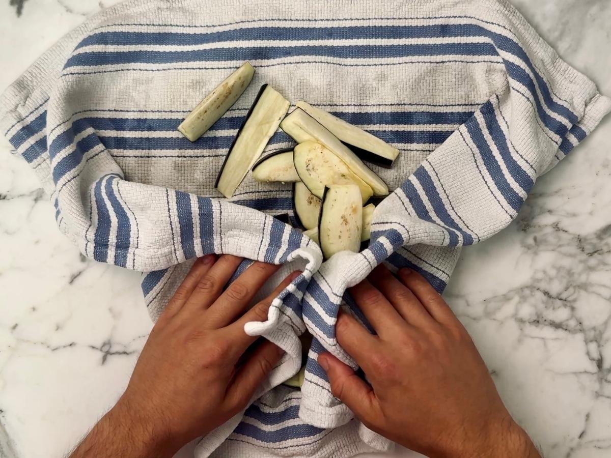 rinsed egglant being dried in a dish towel
