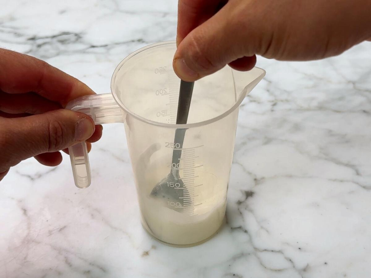 cornstarch being stirred into water with a teaspoon in a jug 