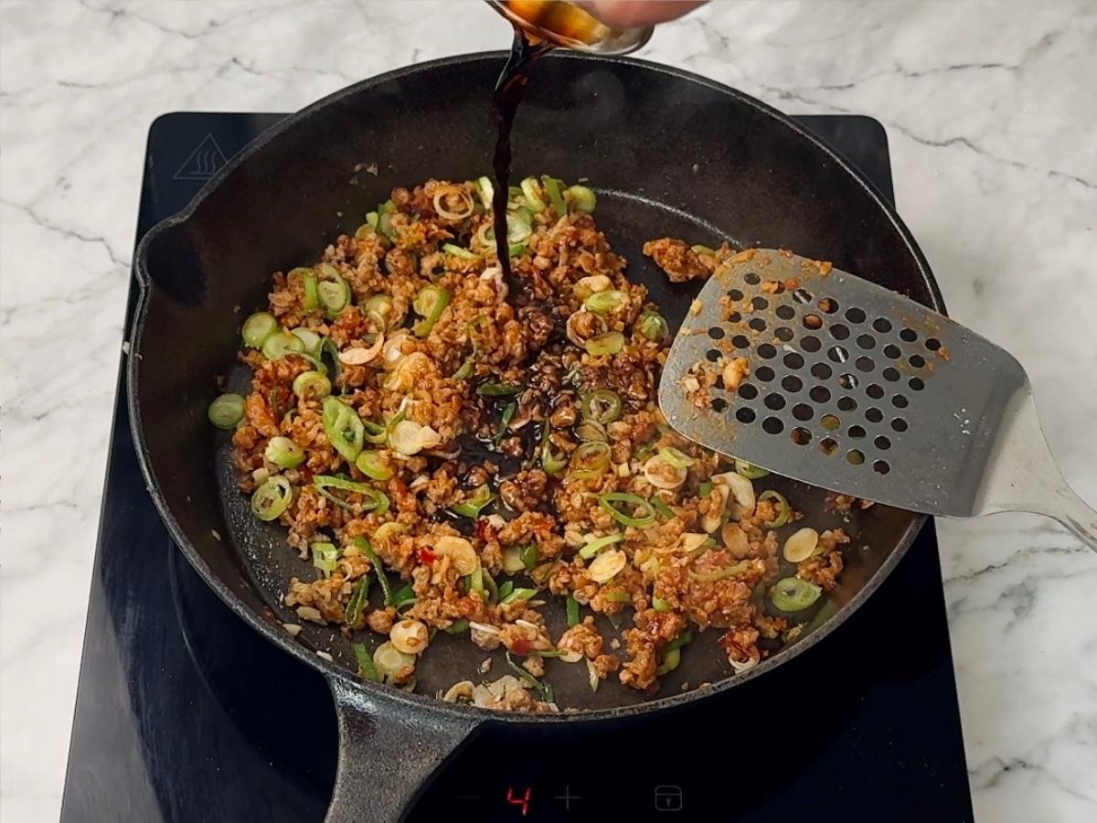 spring onions and sauces being added to the skillet. 
