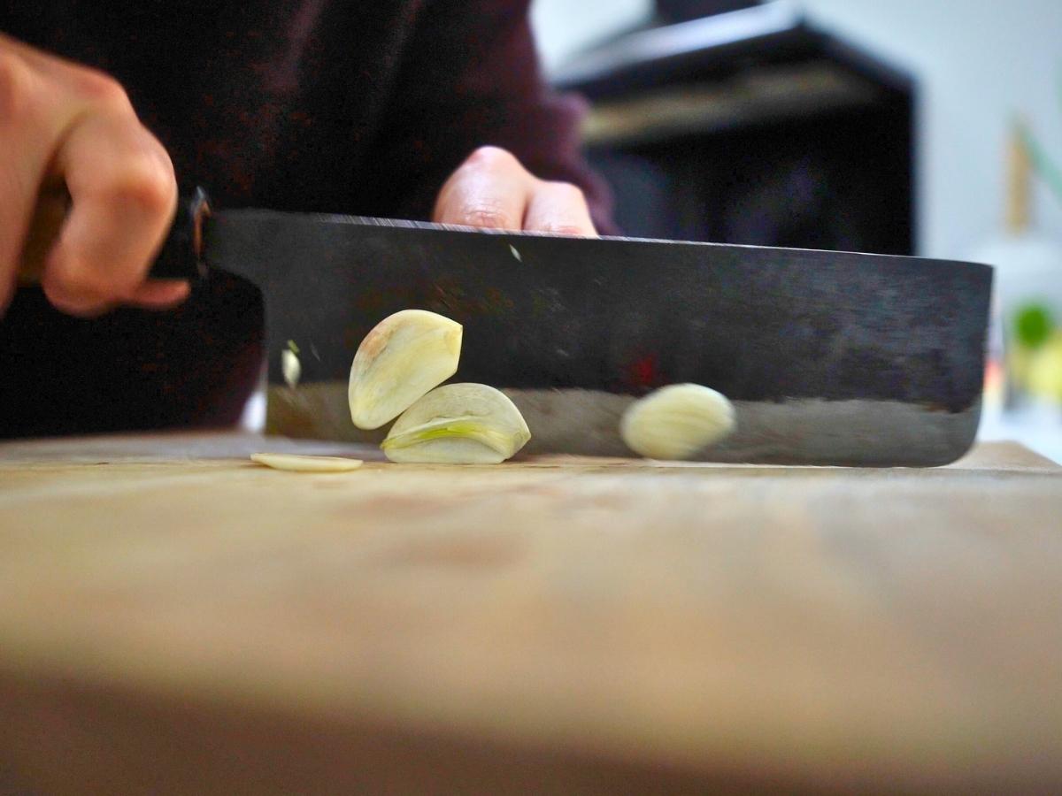 garlic clove being sliced into thin discs
